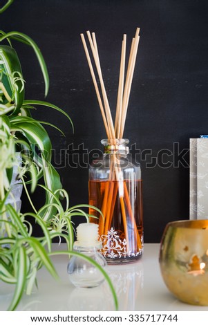 Aroma reed diffuser, candle and spider plant against blackboard wall. Selective focus on bottle and sticks.