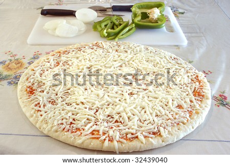 raw uncooked pizza pie with green pepper and onion in the background