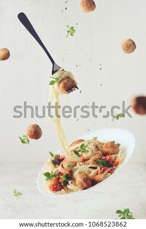 Flying food. Levitation of pasta fettuccine with meatballs, tomato sauce, basil on white concrete background