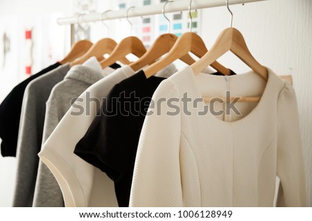 Women dresses new collection of stylish clothes wear hanging on hangers clothing rack rails, fabric samples at background, fashion design studio store concept, dressmaking tailoring sewing workshop