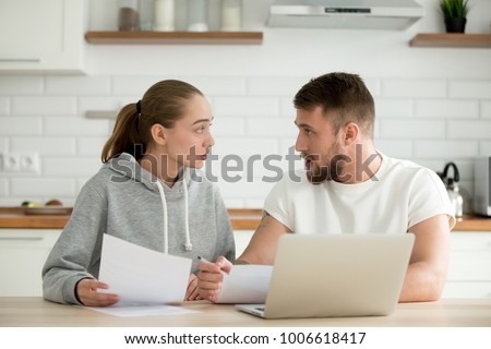 Young unhappy couple arguing about money bills documents at home kitchen, family disputing disagreeing on budget expenses, man and woman quarreling having financial problem with papers and laptop