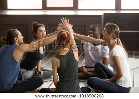 Diverse happy yogi people reach hands to give high five sitting on mats at yoga seminar training, multiracial friends group celebrating unity in fitness goals, supporting motivation for healthy life