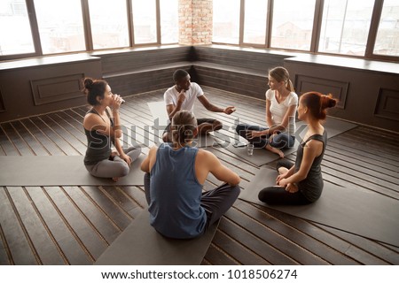 African american yoga instructor talking to diverse group sitting on mat in studio, multiracial happy people having conversation about healthy mindful life and motivation at training seminar class