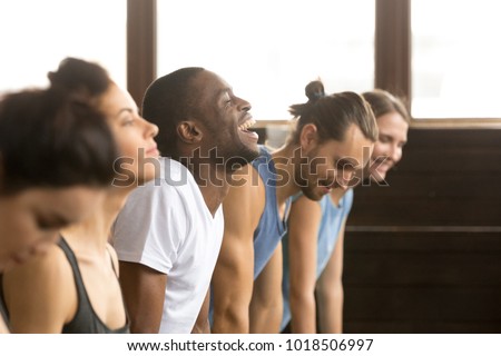 African man beginner laughing having fun trying to do yoga pose, push ups plank or stretching in upward facing dog exercise at group training class with multiracial diverse people, closeup side view