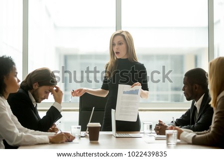 Dissatisfied angry female executive scolding african employee for bad work at diverse group meeting, white woman boss reprimanding black subordinate for poor financial result at office team briefing