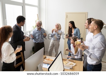 Friendly diverse business team of young and senior colleagues eating pizza together in office, multiracial coworkers staff group talking and laughing at funny joke on lunch time or coffee break