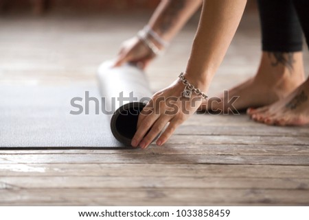 Hands of an attractive young woman folding black yoga or fitness mat after working out at home in living room or in yoga studio. Healthy lifestyle, keep fit, weight loss concepts. Close up view photo