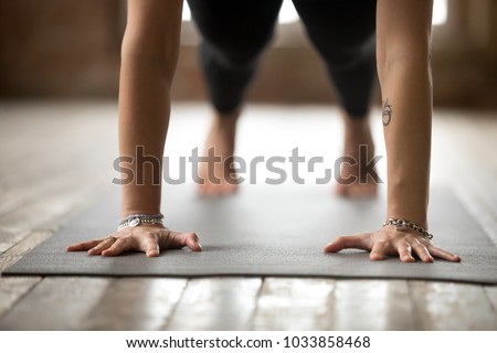 Young sporty woman practicing yoga, doing Push ups or press ups exercise, phalankasana, Plank pose, working out, wearing sportswear, black pants, indoor close up, yoga studio