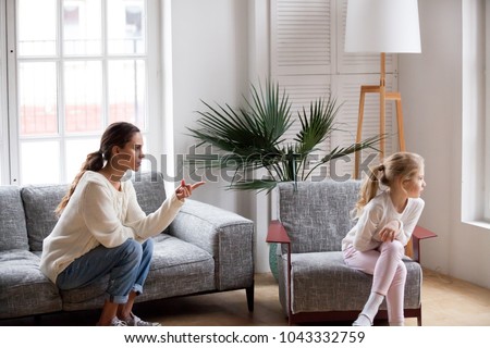 Young strict mother or sister scolding stubborn sulky kid girl in living room at home, offended daughter ignoring angry mom reprimanding disobedient child for bad behavior, family conflict concept