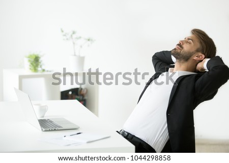 Successful young businessman in suit relaxing at workplace with laptop finished work, relaxed calm employee feels happy breathing fresh air, smiling ceo enjoys break in office, no stress free relief