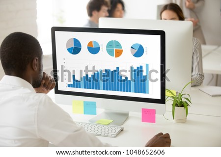 African businessman analyzing graphic data charts graphs of marketing sales project performance on pc monitor in office, black employee preparing statistical report with application or online service