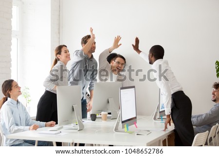 Happy multi-ethnic employees sales team giving high five together celebrating corporate success and good relations, diverse group of office people joining hands excited by common victory achievement