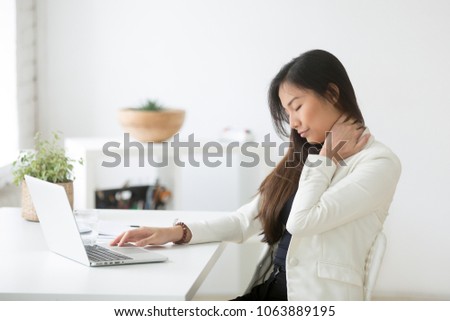 Young asian businesswoman touching massaging stiff neck to relieve pain in muscles after sedentary computer work in incorrect posture, japanese or chinese woman suffering from fibromyalgia at work