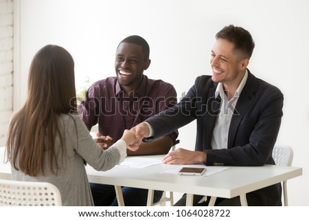 Smiling multiracial hr handshaking female applicant won job interview, friendly diverse executives and successful candidate shaking hands offering employment contract, recruiting and hiring concept