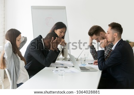 Stressed multiracial team thinking of problem solution at emergency office meeting, sad diverse business people group shocked by bad news, upset colleagues in panic after company bankruptcy concept