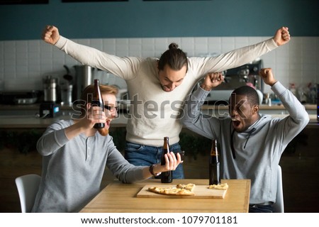 Excited diverse men football fans celebrating victory goal score watching game online on smartphone supporting winning team drinking beer eating pizza together in pub, sport betting win concept
