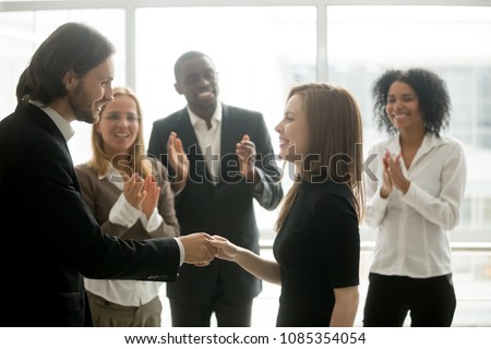 Smiling ceo promoting rewarding handshaking motivating female worker congratulating with promotion or success showing respect while team applauding, appreciation and employee recognition concept