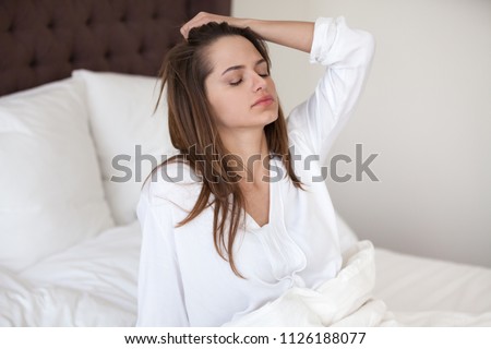 Sleepy young woman feeling drowsy or dizzy after waking up in bed, suffering from lack of sleep deprivation, insomnia, morning headache or migraine, having hangover after sleepless night concept