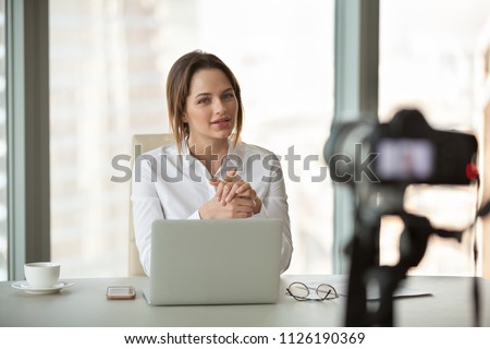 Young businesswoman recording vlog talking to camera in office, successful female business trainer coach filming live video blog giving presentation speaking about online training, vlogging concept