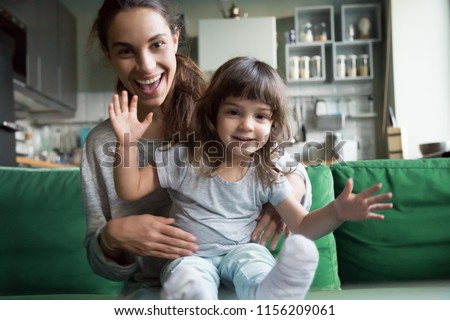 Portrait of happy excited young mother and kid girl waving hands looking at camera, smiling mom with child daughter making video call, family vloggers recording video blog or vlog together concept