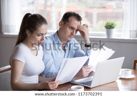 Serious husband and wife reading paper documents analyzing house utility bills, stressed couple get bank notice considering contract terms and conditions, man and woman managing paperwork and finances