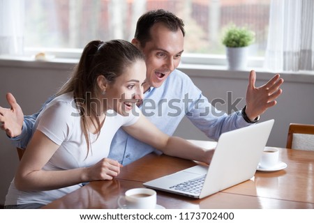 Millennial couple excited reading good news on laptop, happy man and woman screaming winning lottery online cannot believe eyes with success, spouses celebrate victory or achievement, feeling triumph