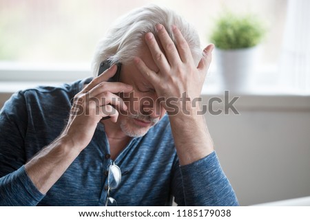 Frustrated older mature retired man feeling upset desperate talking on the phone having problems debt, stressed sad middle aged male depressed by hearing bad news during mobile conversation at home