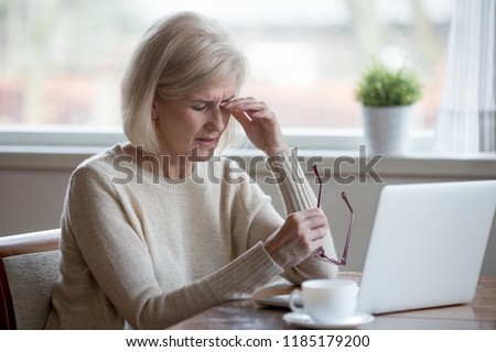 Upset fatigued overworked senior mature business woman taking off glasses tired of computer work, exhausted middle aged employee suffers from blurry vision after long laptop use, eye strain problem