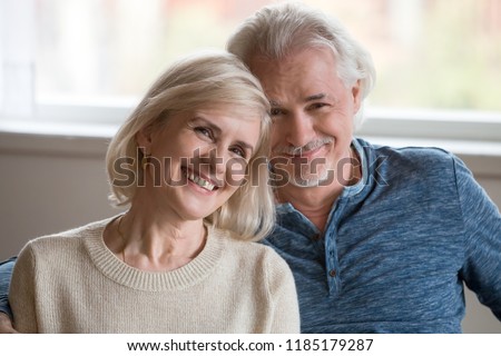 Headshot portrait of happy middle aged romantic couple dating posing indoors, smiling retired old family embracing looking at camera, loving senior mature man and woman hugging bonding together