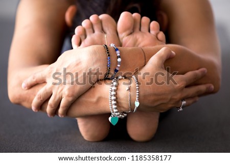 Young sporty woman practicing yoga, doing Seated forward bend, head to knee exercise, paschimottanasana pose, working out, wearing bracelets, indoor close up, at yoga studio