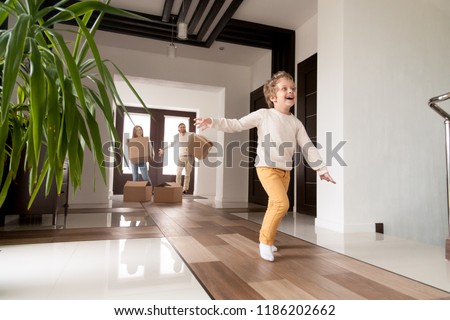 Happy married couple with little preschool son arriving in new house. Millennial first time buyers with cardboard boxes looking at running excited child. Buying real estate, mortgage, moving concept