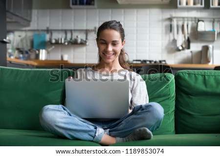 Happy smiling woman sitting on sofa, couch and using laptop at living room at home, watching funny video, learning language, video calling, mother working online