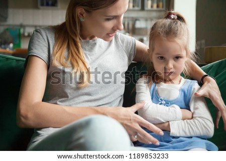 Angry offended little girl ignoring not listening mother words, advice, mum hugging, talking with stubborn, upset daughter at living room, bad upbringing, difficult behavior of child