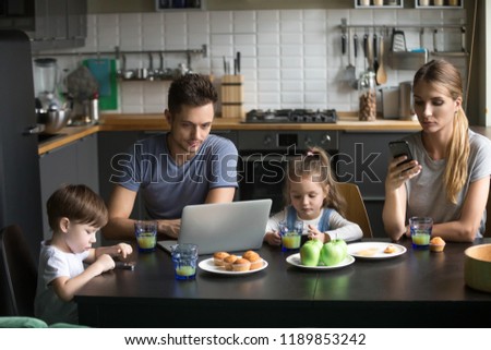 Parents using laptop and smartphones having breakfast with children, bored father writing email, searching internet while mother, son and daughter using phone apps, ignore, family gadget addiction