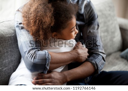Close up African American family daddy and daughter spend time together at home.  Black father embrace sincere little preschool girl sitting on couch. Happy fatherhood loving wellbeing family concept