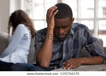 Close up black african couple sitting together not looking at each other on couch in living room at home after quarrel. Sad husband frustrated wife. Break up, problems trouble in relationship concept