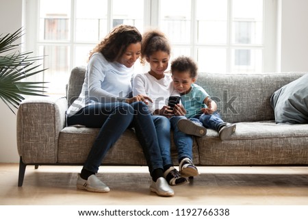 Black family sitting on couch have a fun at home. African mother spend free time with daughter and son using mobile phone taking selfie photo playing new game. Happy family together on weekend concept