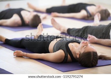 Group of young sporty people practicing yoga lesson, doing Dead Body, Savasana, exercise Corpse pose, working out, indoor, students training in club, studio close up. Well-being concept