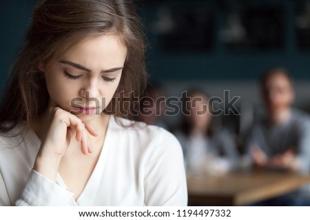 Upset young girl sitting alone in café offended at friends joke, sad millennial woman suffer from low self-esteem, depressed female outcast feeling outsider hanging out with company in coffeeshop