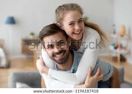Head shot happy millennial young man and woman hugging embracing indoors. Portrait close up smiling husband and wife piggyback ride looking at camera laughing. Dating and romantic relationship concept