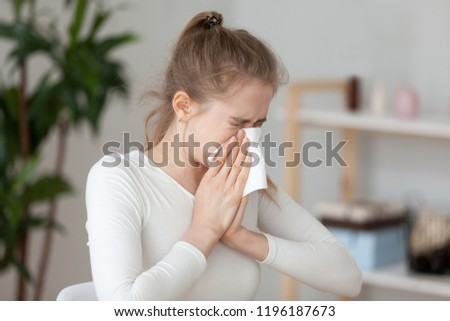Young millennial sick woman sitting alone at work office sneeze holding tissue handkerchief and blowing wiping her running nose. Student girl has seasonal allergy or chronic sinusitis disease concept