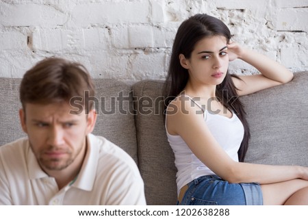 Offended frustrated girlfriend looking at sitting separately sad boyfriend, young couple having relationships problem, difficulties, not talking after quarrel, man avoid looking or speaking to woman