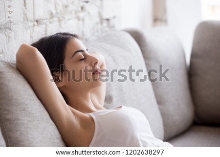 Young calm woman relaxing leaning back with hands behind head on comfortable sofa, having daydream, tired girl sleeping, napping on couch in living room, breathing calm, no stress free weekend at home