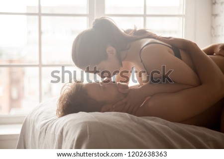 Sensual loving couple lying in bed, embracing with closed eyes, attractive woman kiss man nose, girlfriend on top of boyfriend enjoying intimate moment, having tender foreplay before making love, sex