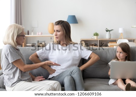 Little girl watch mother and grandmother argue at home, having dispute or disagreement, small daughter busy with laptop see mom crying quarrelling with granny, child witness adult conflict