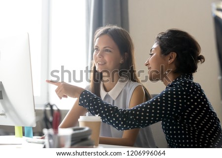 Smiling millennial diverse colleagues discussing online work together, happy caucasian female intern listening to indian mentor explaining computer task training employee, office mentoring concept