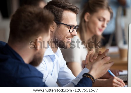 Close up of male colleagues cooperating in coworking office space talking laughing together, smiling man workers chat at workplace, discussing something having fun, employees joke while working at pc