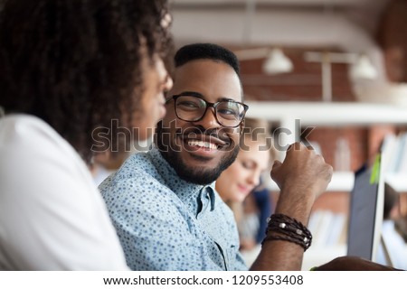 Close up of smiling African American employee look at female colleague chatting in office, happy black male worker talk with woman coworker, having casual conversation at workplace, have fun