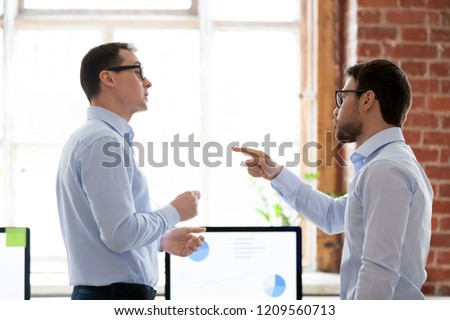 Mad male colleagues have disagreement in office arguing on work issues, furious millennial employee point at coworker blaming for mistake or failure, businessman accuse partner disputing at workplace