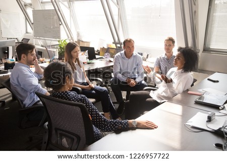 African female leader coach mentor teacher speaking to team workers interns explaining new project discussing corporate business plan at multiracial group office meeting or sales corporate training